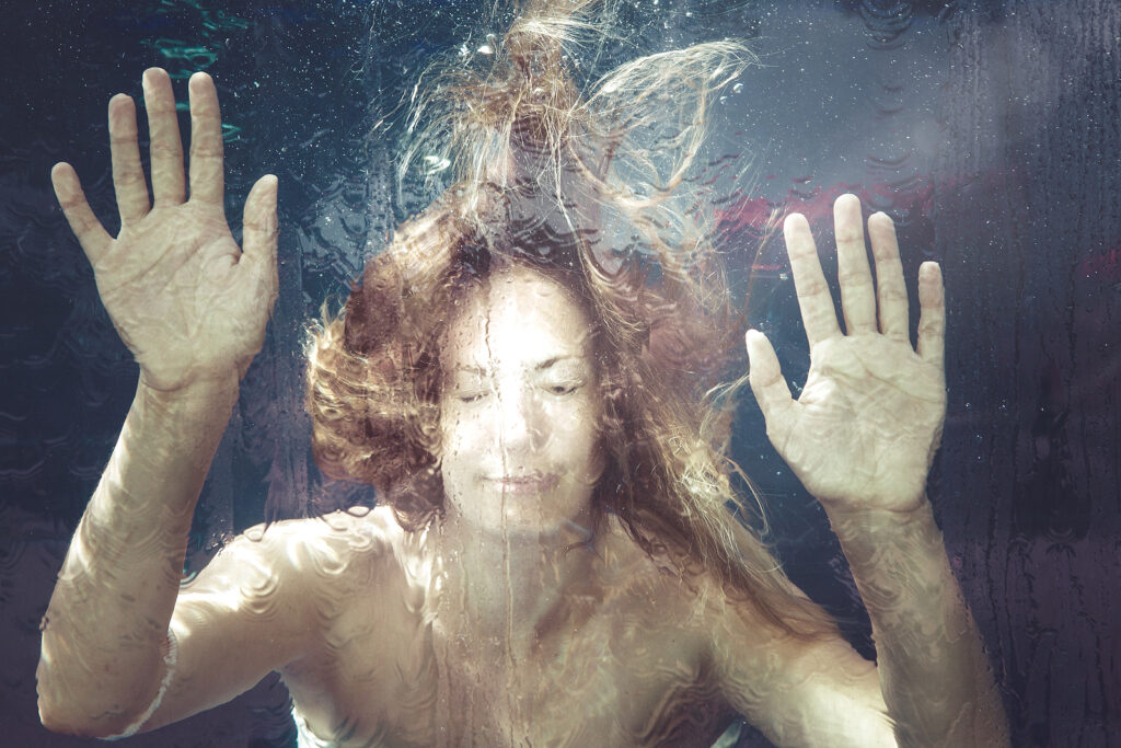 Eine Frau, die im Wasser hinter einer Glaschheibe taucht