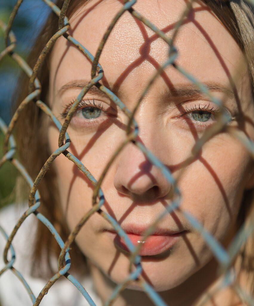 Eine junge Frau blickt durch einen Maschendrahtzaun.