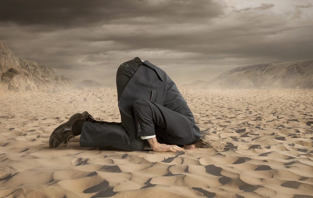 Ein Mann im Anzug, der seinen Kopf in den Sand steckt